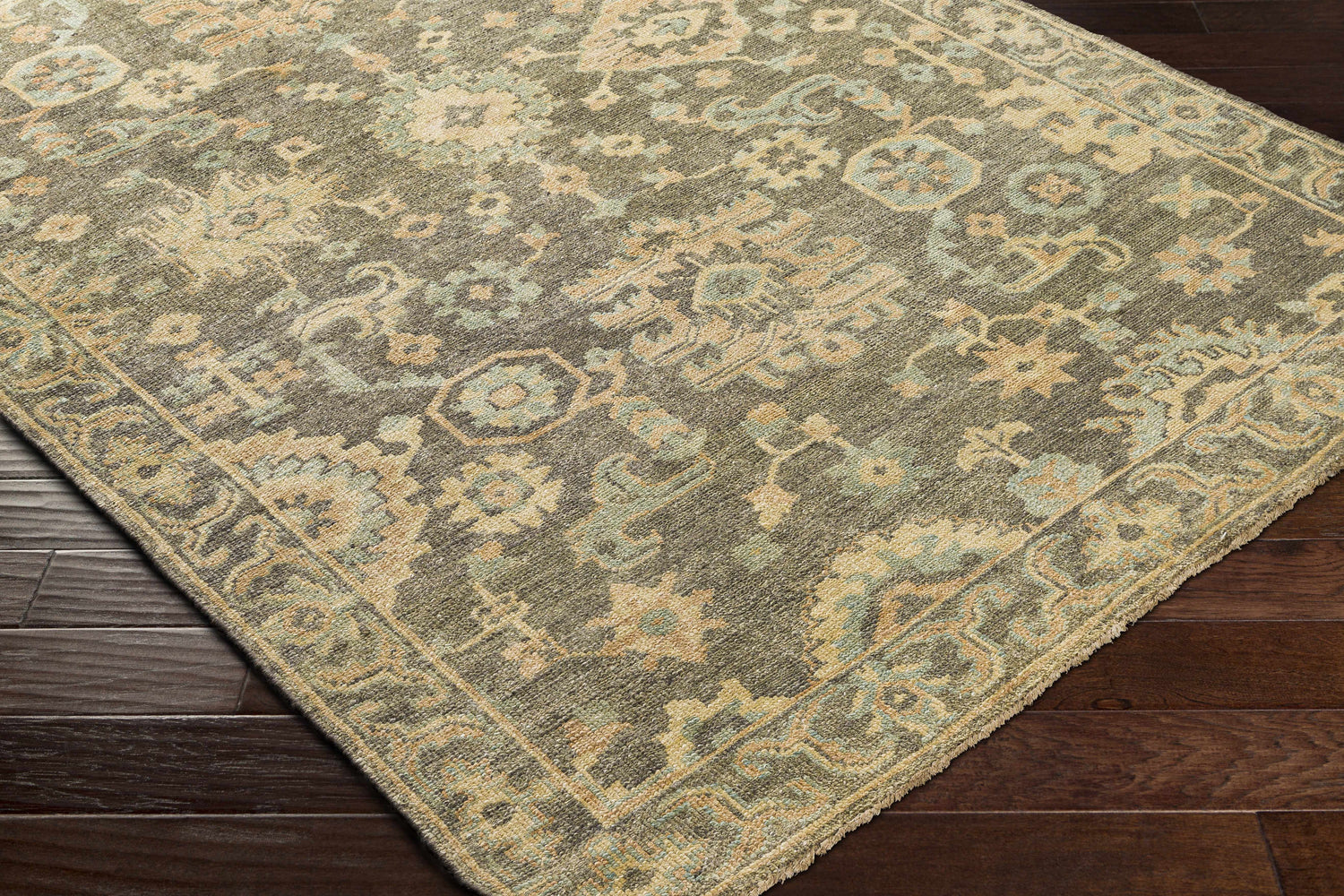 Close-up of the hand-knotted Asotin Area Rug. Wool rug with burnt orange, charcoal, mustard, olive, and seafoam colors. Corner