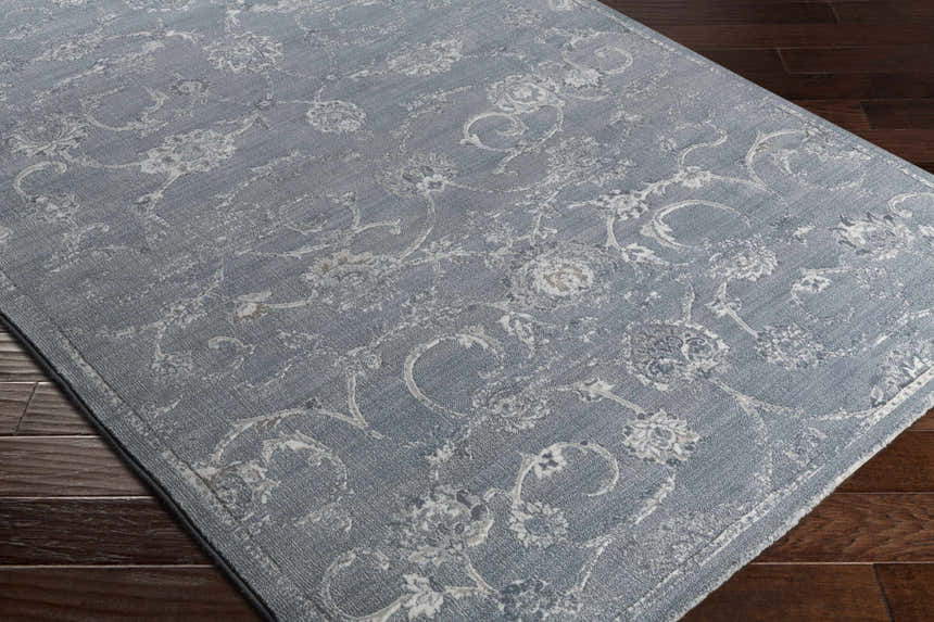Close-up of the Astatula Area Rug. Blue rug with ice blue and ivory floral pattern on dark wood floor. Corner