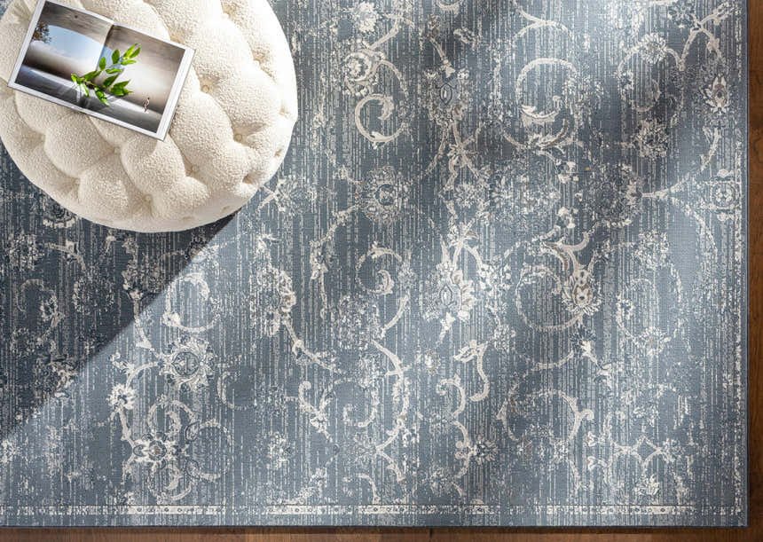 Close-up of blue Astatula Area Rug with ivory floral pattern and texture, styled with a tufted ottoman. Styleshot