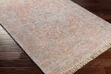 Close-up of the hand woven Atulayan Premium Rug. Bohemian style rug in blue, coral, and gray on dark wood floor. Corner