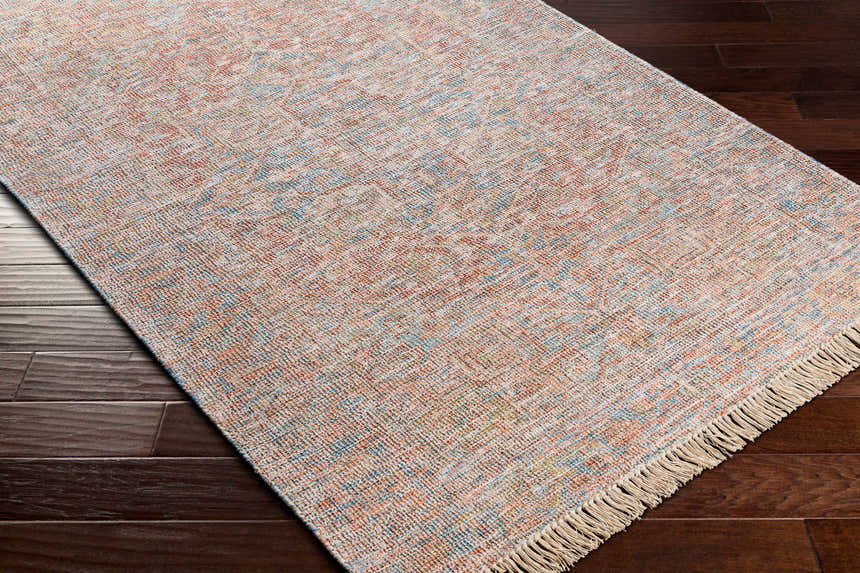 Close-up of the hand woven Atulayan Premium Rug. Bohemian style rug in blue, coral, and gray on dark wood floor. Corner