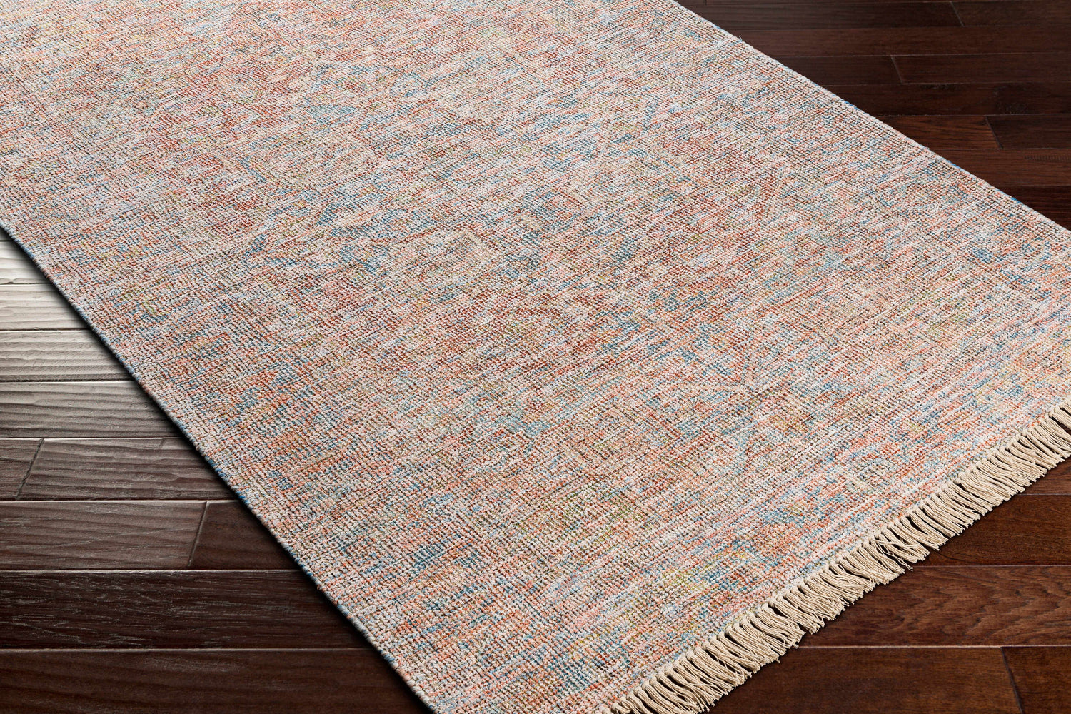 Close-up of the hand woven Atulayan Premium Rug. Bohemian style rug in blue, coral, and gray on dark wood floor. Corner