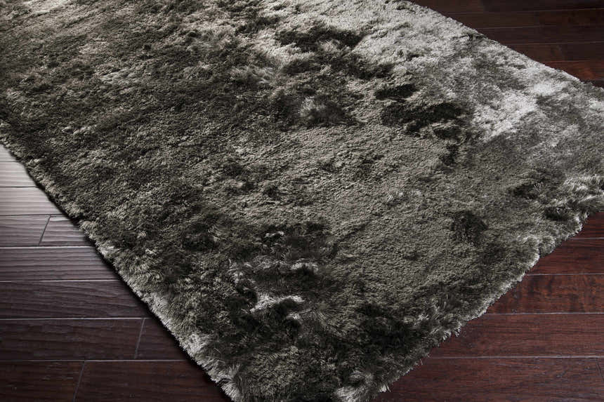 Close-up of a teal and ink blue Auxier Area Rug showing its shag texture on dark wood flooring. Corner