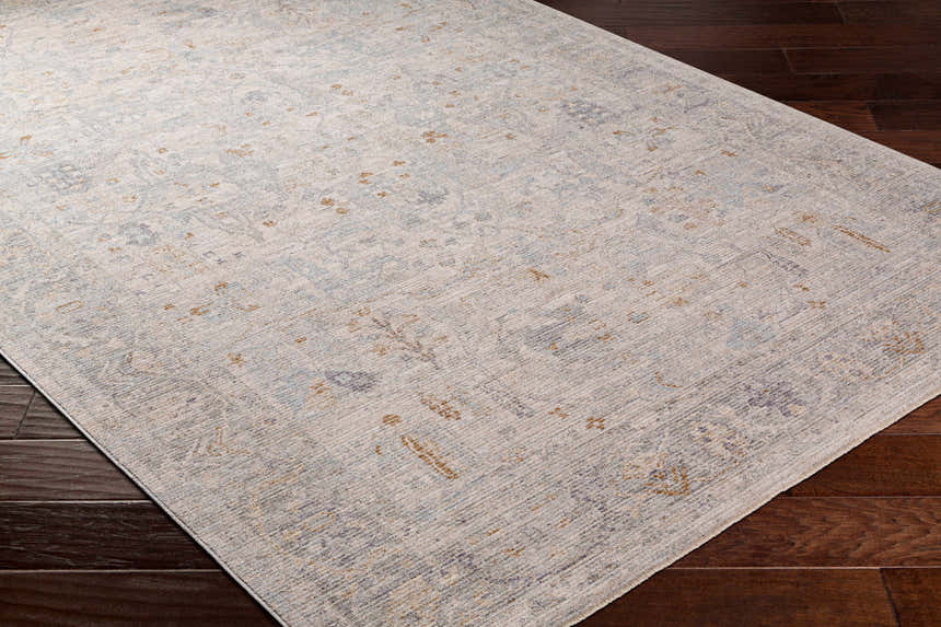 Close-up of Ayarn Thick Luxe Statement Rug in brown, charcoal, teal, sage, and gray on dark wood floor. Traditional style. Corner