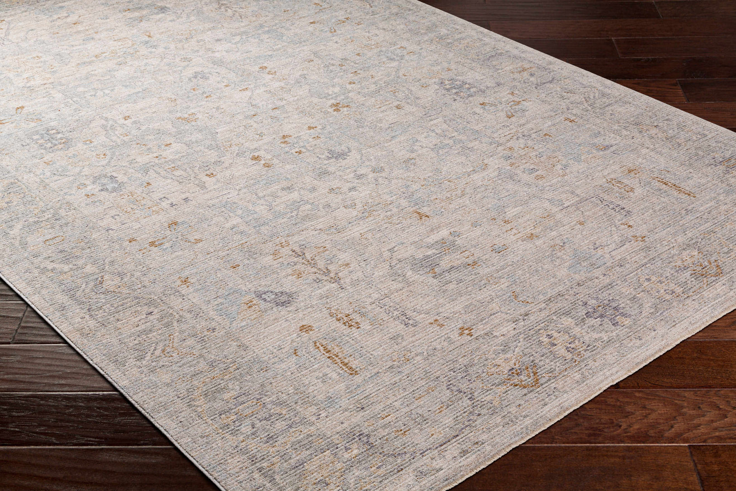 Close-up of Ayarn Thick Luxe Statement Rug in brown, charcoal, teal, sage, and gray on dark wood floor. Traditional style. Corner