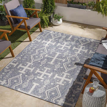 Outdoor patio scene with Bagenalstown rug in dark gray and white, surrounded by wooden chairs and potted plants. Roomscene-Rectangle