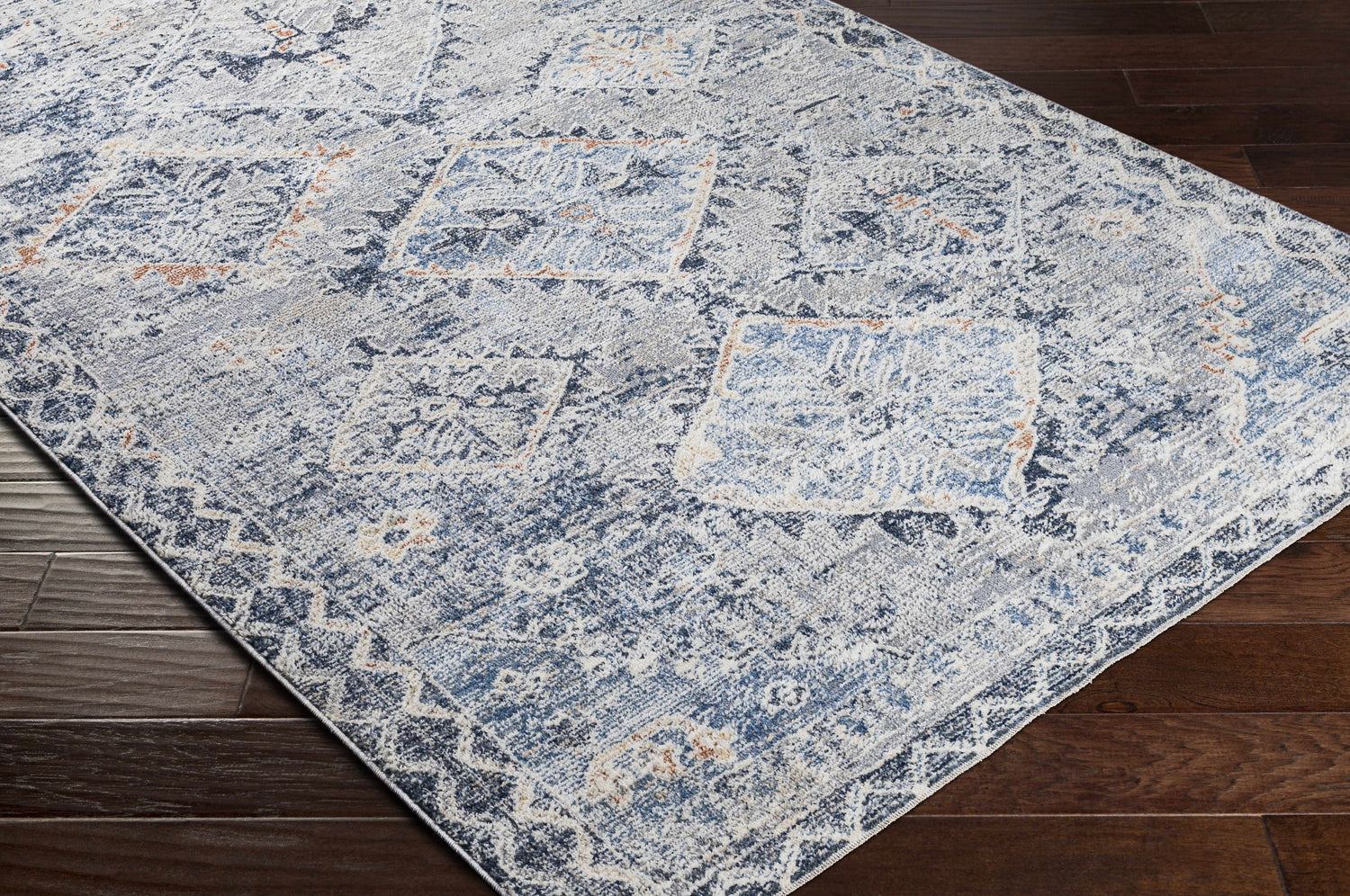 Close-up of the Balamban Area Rug. Features a blue, cream, and beige bohemian pattern on a dark wood floor. Corner