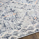 Close-up of the Balamban Area Rug showing its brick red, cream, denim, and gray bohemian pattern and soft polyester texture. Texture