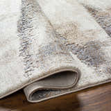 Close-up of the Banji Abstract Waves Area Rug showing its beige, gray, and brown textured pattern and machine-woven construction. Fold