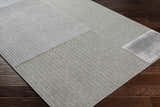 Close-up of the Bantiqui Area Rug showing a geometric pattern and texture on dark wood flooring. Corner
