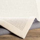 Close-up of the hand-tufted Barrow Wool Rug. Cream and light gray textured weave with a solid cream border. Fold