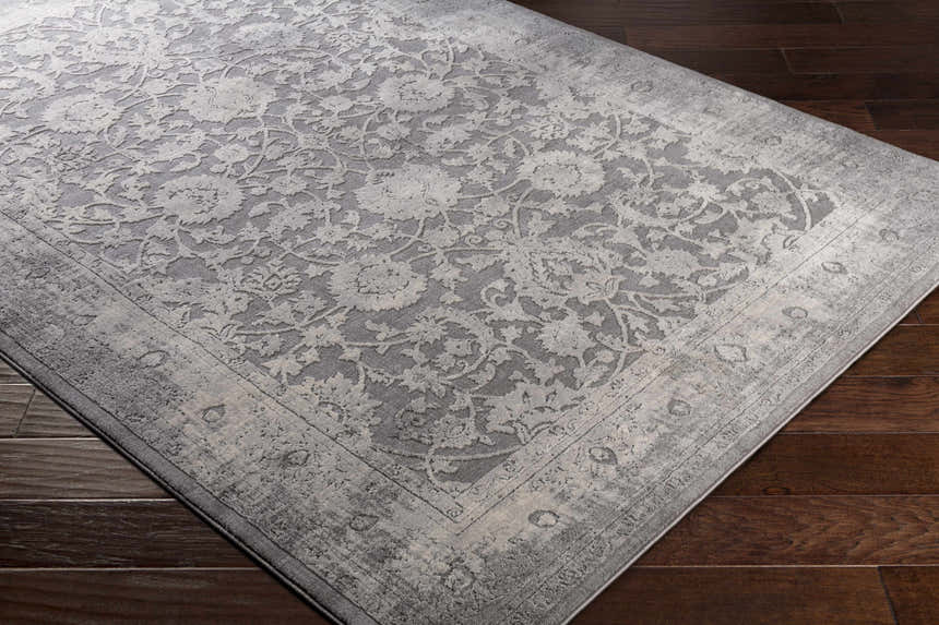 Close-up of the Benavides Gray Updated Traditional Tibetan Rug. Floral design in charcoal, gray, and ivory on dark hardwood floor. Corner