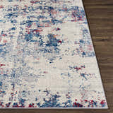 Close-up of the Bergvliet Area Rug showing its cream base with blue and burgundy abstract pattern on a dark wood floor. Front