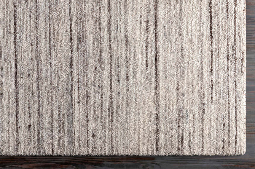 Close-up of the hand-loomed Beykoz Area Rug. Cream and light beige rug with dark brown vertical stripes. Contemporary style. Corner