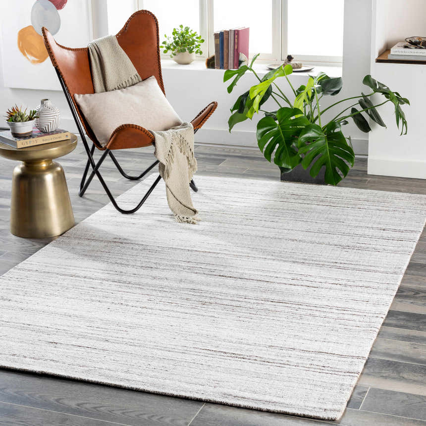 Living room scene with a cream and brown Beykoz Area Rug, tan leather chair, and gray wood floors. Roomscene-Rectangle