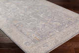 Close-up of Binx rug showing traditional pattern in brown, charcoal, dusty sage, medium gray, and teal on dark wood floor. Corner