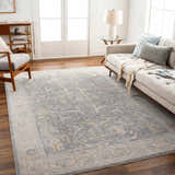Living room scene with a gray sofa and the Binx Thick Luxe Statement Rug in brown, charcoal, dusty sage, medium gray, and teal. Roomscene-Rectangle
