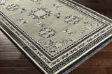 Close-up of the hand-knotted Bixby Area Rug. Wool rug with black, sage green, and beige floral and geometric pattern. Corner