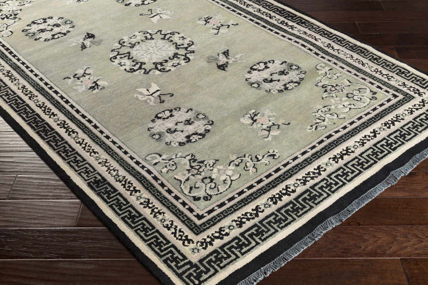 Close-up of the hand-knotted Bixby Area Rug. Wool rug with black, sage green, and beige floral and geometric pattern. Corner