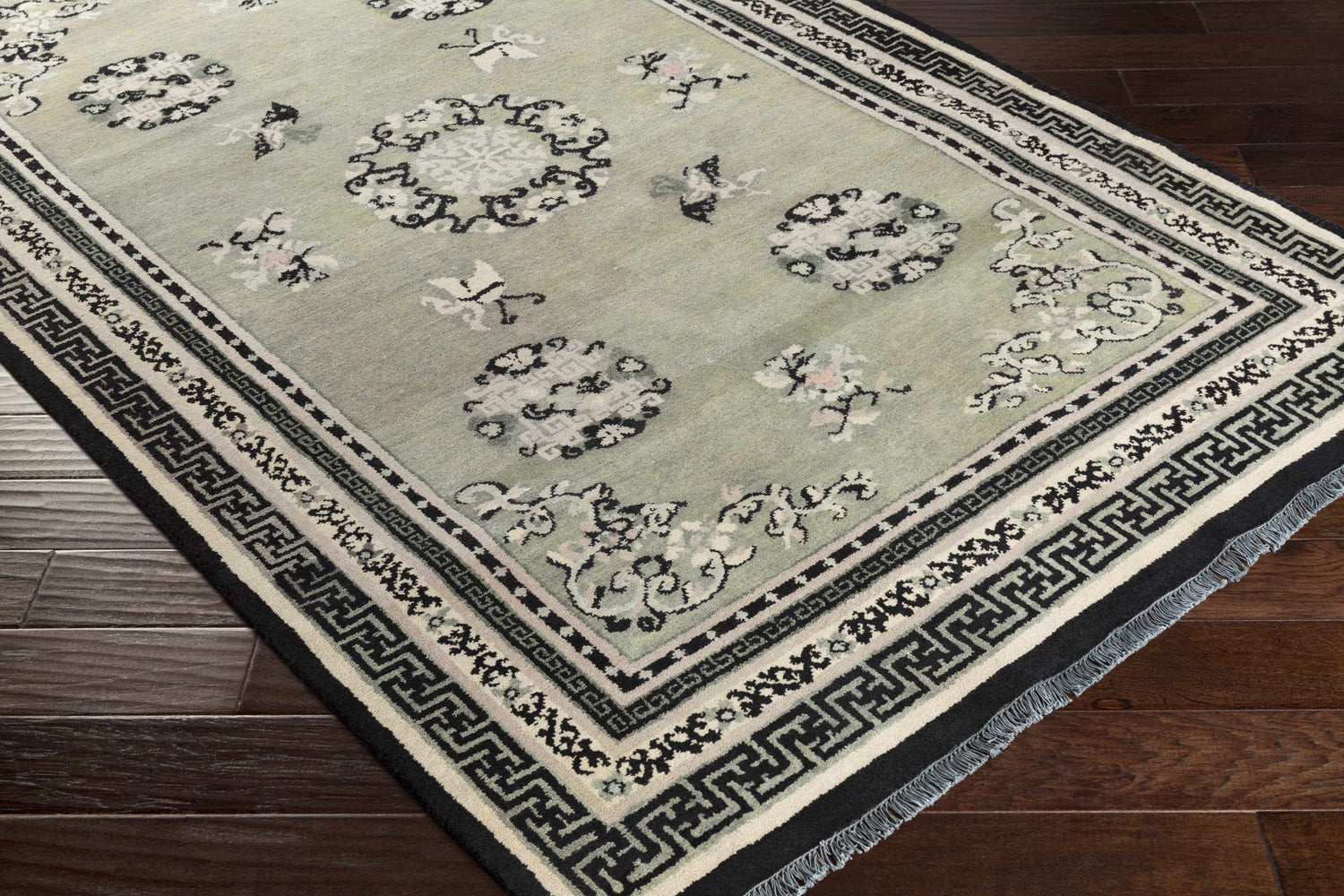 Close-up of the hand-knotted Bixby Area Rug. Wool rug with black, sage green, and beige floral and geometric pattern. Corner