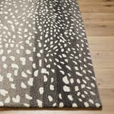 Close-up of the Athena Giraffe Print Wool Rug. Beige and charcoal tones with a spotted pattern on wood floor. Front