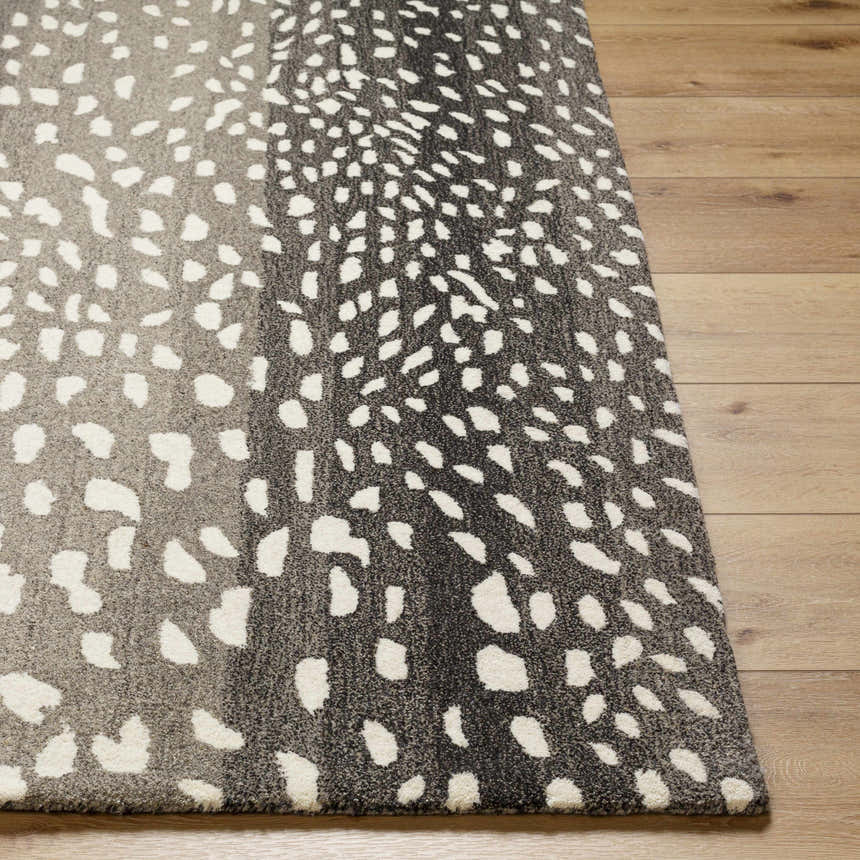 Close-up of the Athena Giraffe Print Wool Rug. Beige and charcoal tones with a spotted pattern on wood floor. Front