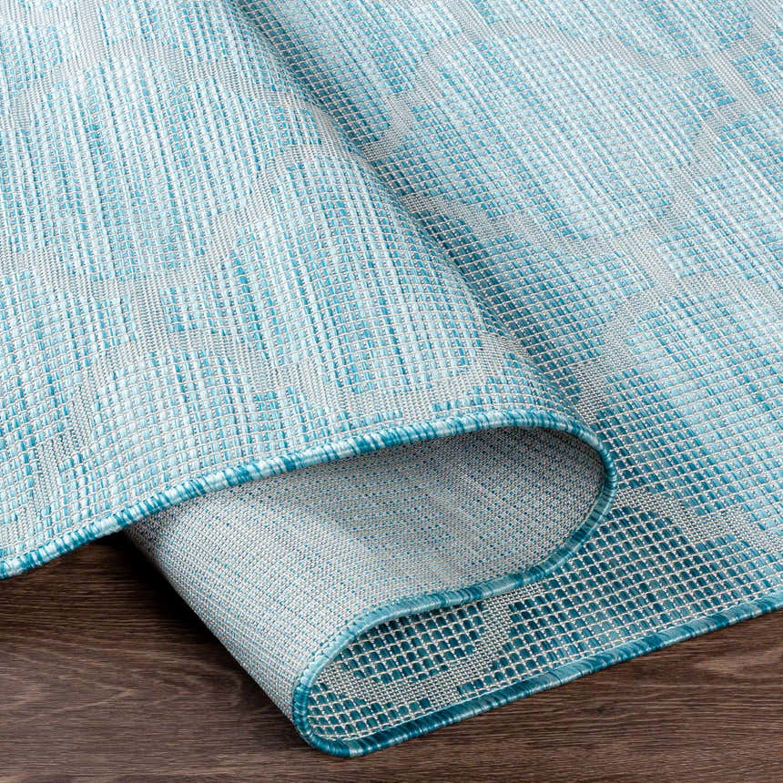 Close-up of the Unique Outdoor Trellis Area Rug, Aquamarine. Features a textured, woven trellis pattern in aqua and light gray. Fold