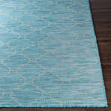 Close-up of the Unique Outdoor Trellis Area Rug, Aquamarine, with a geometric trellis pattern on a dark wood floor. Front