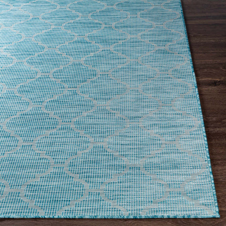 Close-up of the Unique Outdoor Trellis Area Rug, Aquamarine, with a geometric trellis pattern on a dark wood floor. Front