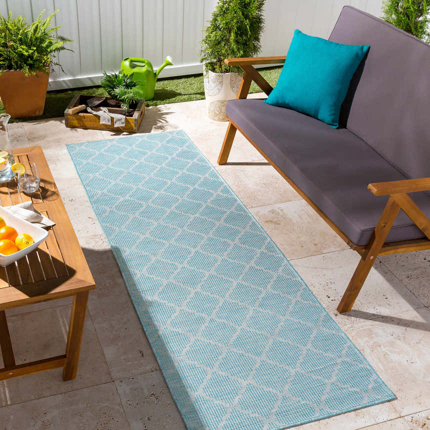 Outdoor patio scene with an aquamarine Unique Outdoor Trellis Area Rug, wooden furniture, and potted plants. Roomscene-Runner