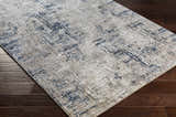 Close-up of the Balasing Area Rug on dark wood floor. Abstract design with dark gray, ivory, and tan colors. Contemporary style. Corner