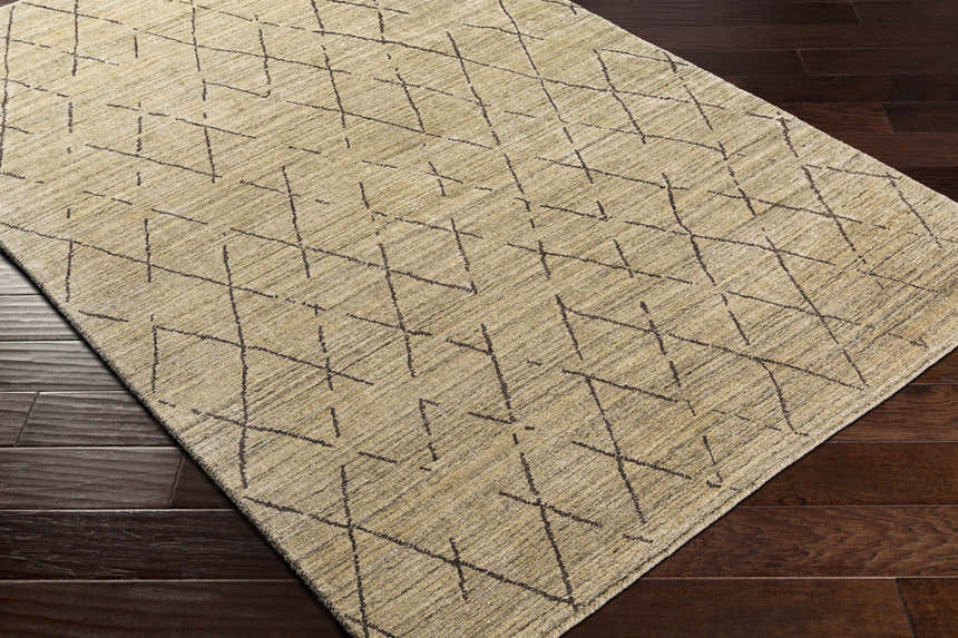 Close-up of the hand-loomed Bonogin Area Rug. Dark brown geometric pattern on a tan and olive viscose rug. Corner