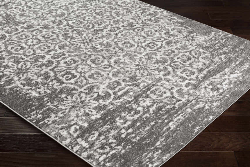 Close-up of the Bowden Carpet - Clearance. Charcoal, light gray, and white floral pattern rug on dark wood floor. Corner