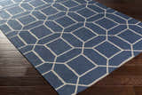 Close-up of the Bowdon Area Rug. Navy rug with a white geometric pattern on dark wood flooring. Corner