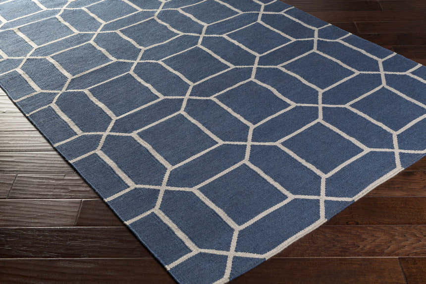 Close-up of the Bowdon Area Rug. Navy rug with a white geometric pattern on dark wood flooring. Corner
