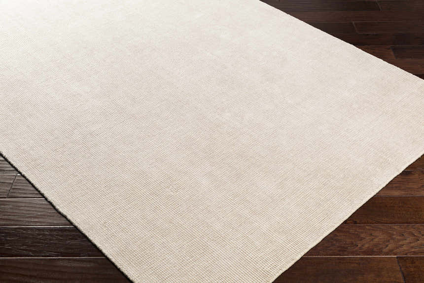 Close-up of the hand-loomed Bowstring Carpet. Cream and taupe viscose rug with subtle texture on dark wood floors. Corner