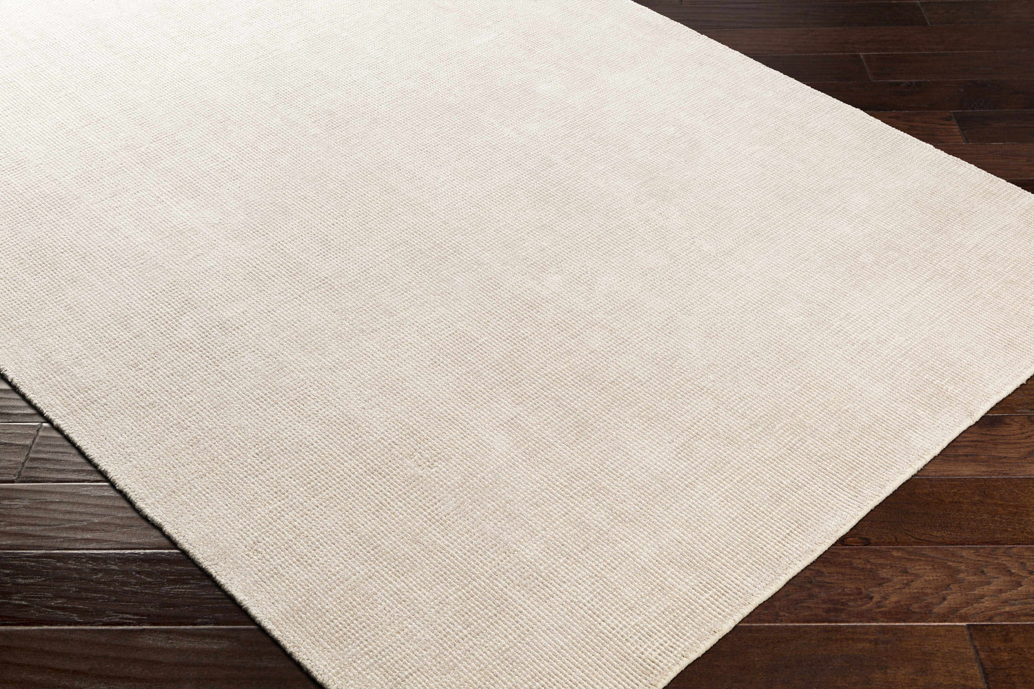 Close-up of the hand-loomed Bowstring Carpet. Cream and taupe viscose rug with subtle texture on dark wood floors. Corner