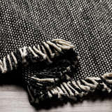 Close-up of the Boyden Black Area Rug with Tassels. Hand-woven texture in black and cream recycled yarn, with knotted fringe. Fold