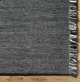 Close-up of the hand-woven Boyden Black Area Rug with Tassels, showing black, cream, and gray yarns and tassel detail. Corner