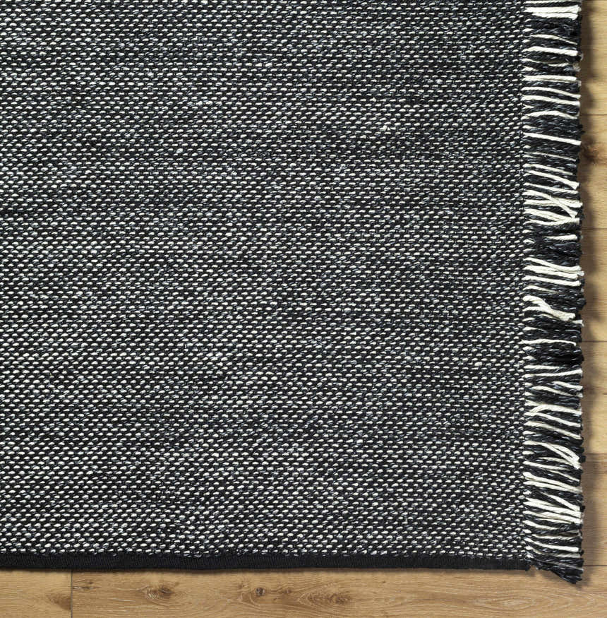 Close-up of the hand-woven Boyden Black Area Rug with Tassels, showing black, cream, and gray yarns and tassel detail. Corner