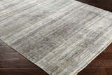 Close-up of the Braxton Carved Statement Area Rug showing its gray, ivory, and brown linear pattern and texture on dark wood floors. Corner