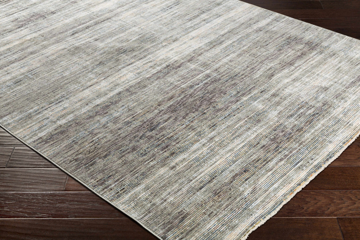 Close-up of the Braxton Carved Statement Area Rug showing its gray, ivory, and brown linear pattern and texture on dark wood floors. Corner