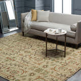 Living room scene with a traditional Brentford Carpet in oatmeal, brown, and olive tones. Wool rug complements the gray sofa and walls. Roomscene-Rectangle