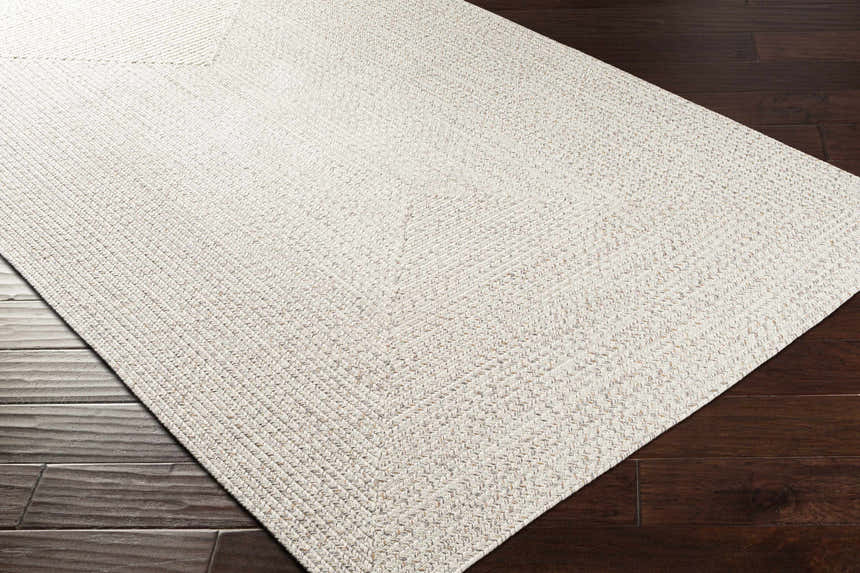 Close-up of Beige Braided Faux Jute Rug showing texture and braided design on dark wood floors. Corner