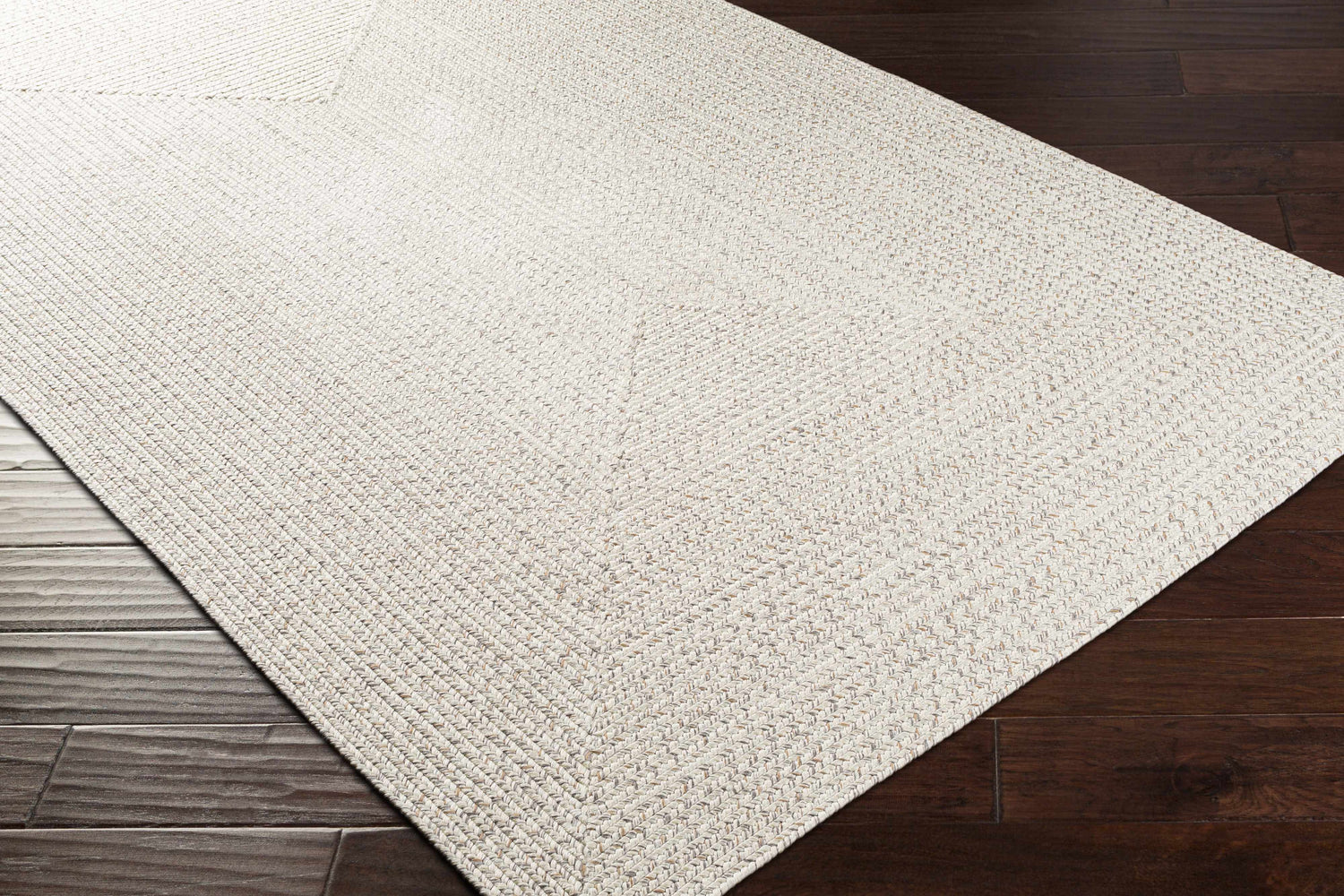 Close-up of Beige Braided Faux Jute Rug showing texture and braided design on dark wood floors. Corner