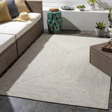Outdoor patio with beige Braided Faux Jute Rug, brown wicker furniture, and neutral decor. Roomscene-Rectangle