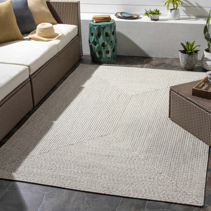 Outdoor patio with beige Braided Faux Jute Rug, brown wicker furniture, and neutral decor. Roomscene-Rectangle