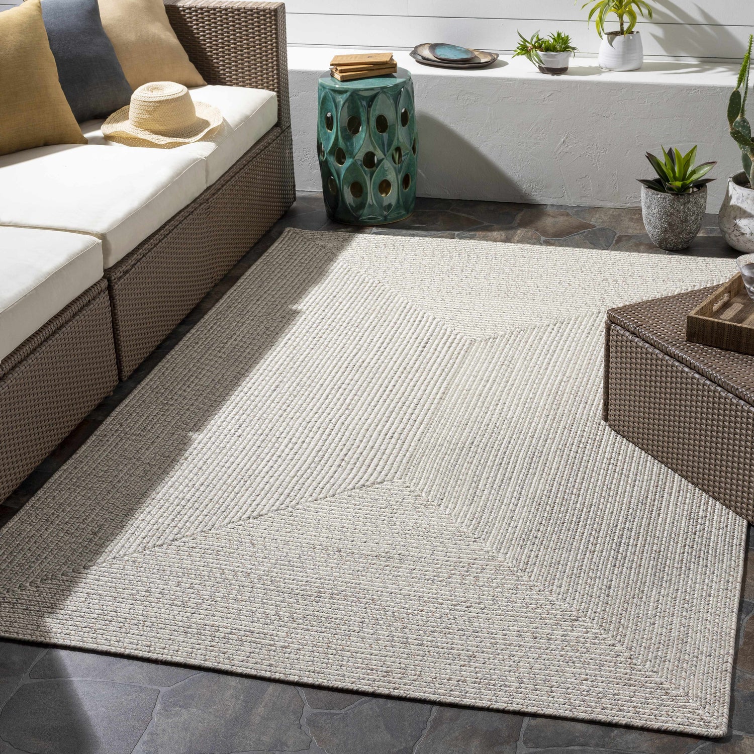 Outdoor patio with beige Braided Faux Jute Rug, brown wicker furniture, and neutral decor. Roomscene-Rectangle