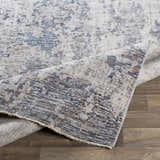 Close-up of the Broxbourne Area Rug, showing its abstract pattern in denim, taupe, and cream colors. Fold