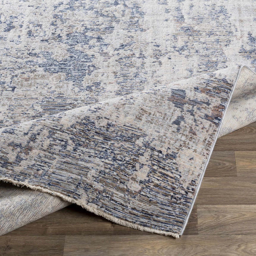 Close-up of the Broxbourne Area Rug, showing its abstract pattern in denim, taupe, and cream colors. Fold